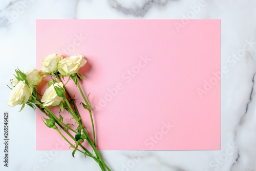Wedding invitation card. Rose flowers and blank pink paper card on marble background. Wedding concept. Flat lay, top view, overhead, copy space
