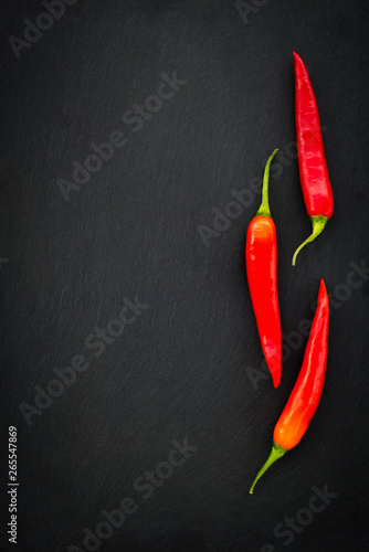 Three red chili peppers on dark background
