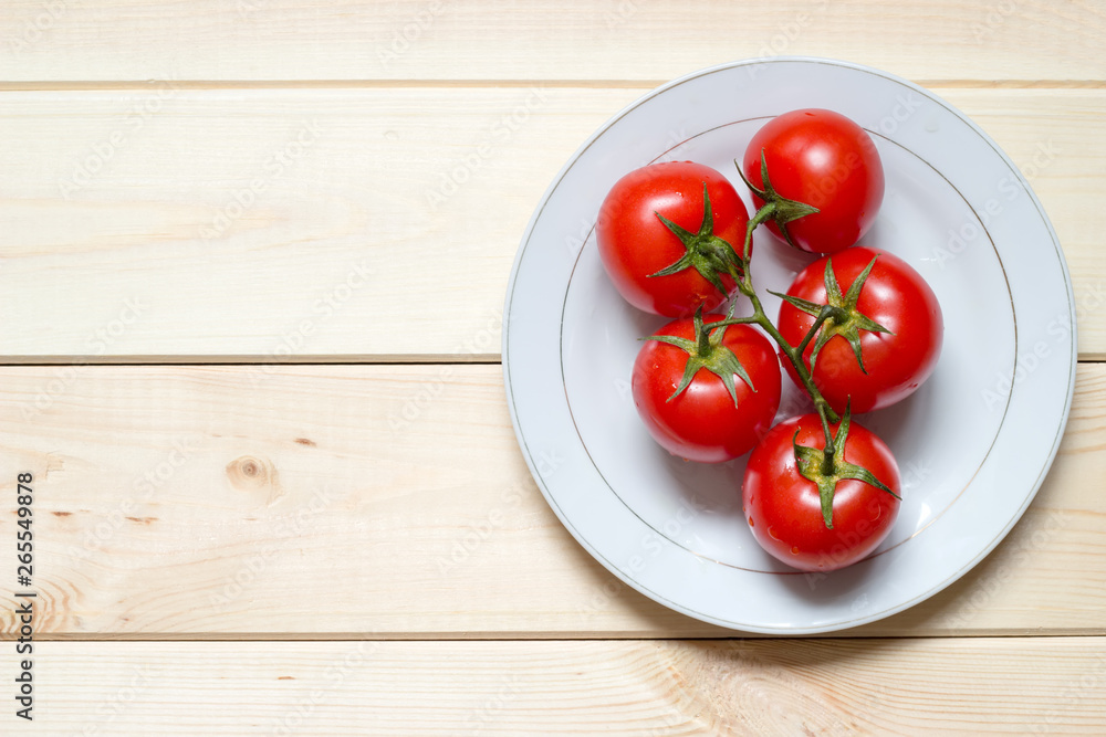 Ripened tomatoes on white plate on light wooden table with copy space Ripened tomatoes on white plate on light wooden table with copy space