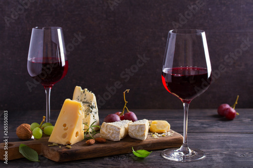 Fototapeta Naklejka Na Ścianę i Meble -  Glasses of wine with cheese, grapes, and nuts on black wooden table. Wine and food