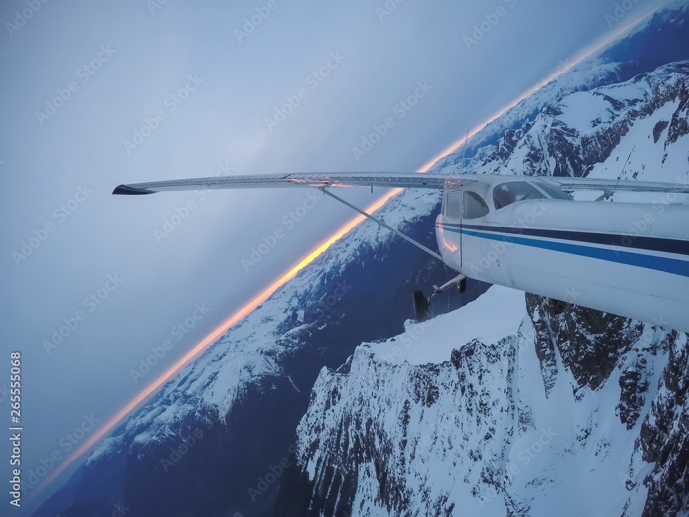Obraz premium Aerial view of a small airplane flying over the Canadian Mountain Landscape during a gloomy cloudy sunset. Taken near Squamish, North of Vancouver, British Columbia, Canada.