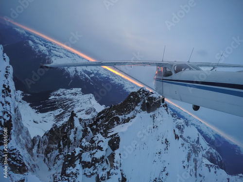 Aerial view of a small airplane flying over the Canadian Mountain Landscape during a gloomy cloudy sunset. Taken near Squamish, North of Vancouver, British Columbia, Canada.
