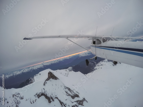Aerial view of a small airplane flying over the Canadian Mountain Landscape during a gloomy cloudy evening. Taken near Squamish, North of Vancouver, British Columbia, Canada.
