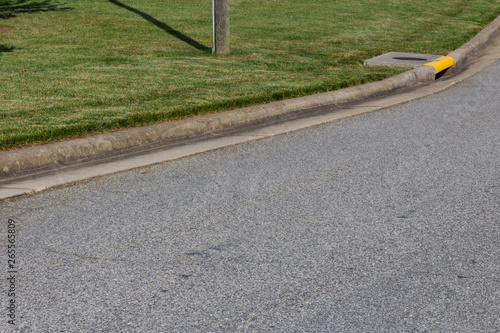 Generic street and sweeping curb, green grass and yellow drain, horizontal aspect