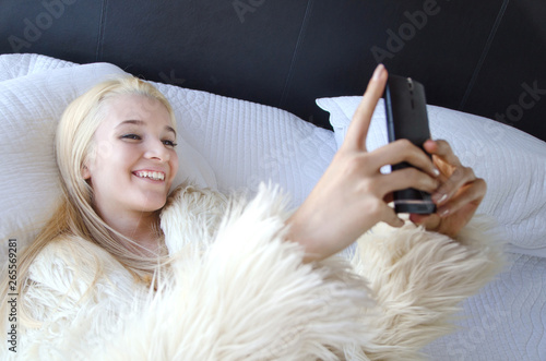 Young lady laying on a bed laughing and taking a selfie