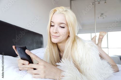 Young lady laying on a bed smiling and looking at her cell phone