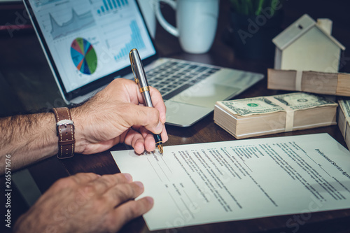 businessman's hand signing agreement with background of moneys and business chart on table