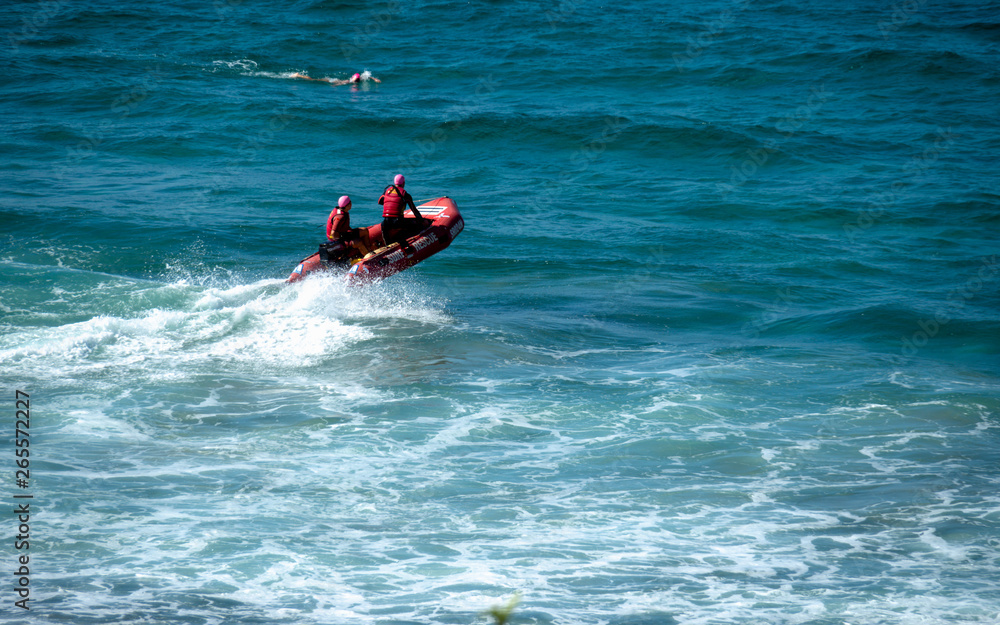 Beach rangers on a red rescue boat a surfer swimming nearby