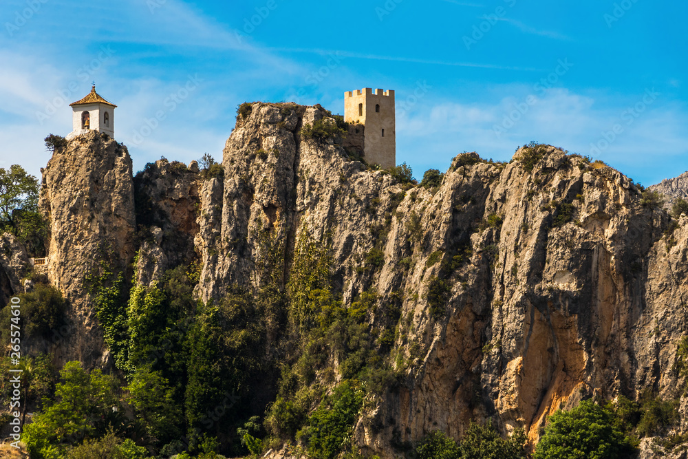 The fort of Guadalest in Spain with buildings on several rocks in sunshine and blue sky.