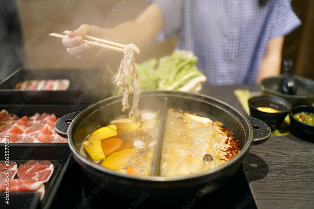 Holding sliced pork using chopsticks on hot pot with smoke for Japanese hot pot also known as Shabu Shabu or Sukiyaki is Japanese style. Holding sliced pork using chopsticks on hot pot with smoke for Japanese hot pot also known as Shabu Shabu or Sukiyaki is Japanese style.