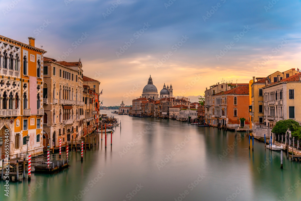 Beautiful landscape sunset view of traditional Gondolas on famous Canal Grande with historic Basilica di Santa Maria della Salute in the background in romantic golden evening light at sunset in Venice