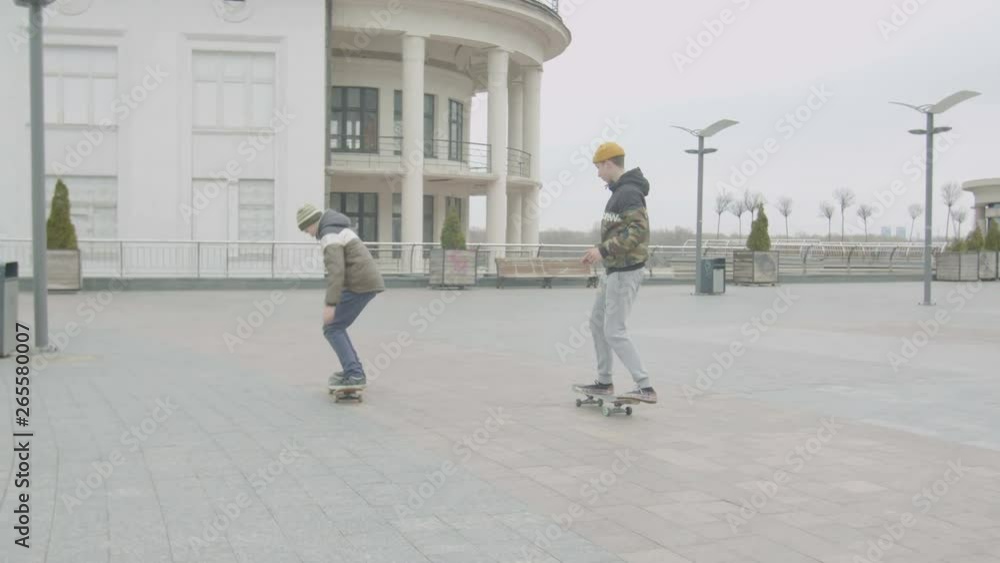 Teenage skaters learning to do rolling off a drop and manual tricks skateboarding on city street. Warmly dressed teenage beginners practicing manual, doing hops and rolling off drop skating outdoors. Teenage skaters learning to do rolling off a drop and manual tricks skateboarding on city street. Warmly dressed teenage beginners practicing manual, doing hops and rolling off drop skating outdoors.