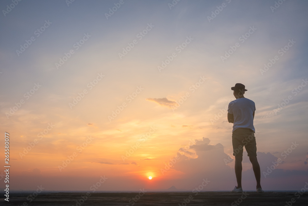 Fototapeta premium Traveler young man standing in the summer mountains at sunset and enjoying view of nature.