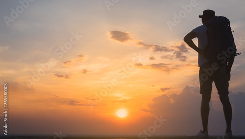 Traveler with backpack watching amazing sunset. Silhouette of the young man on the mountain top
