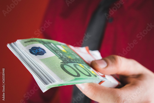 man in red suit holds out a wad of money in his hand on red background