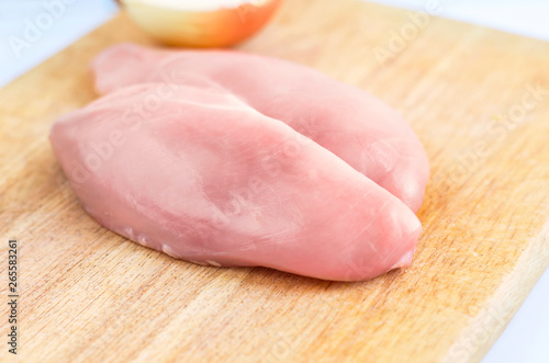 Raw Chicken Breasts, Fillets on a Wooden Cutting Board with Half Onion On White Background. Healthy Organic Food, Poultry Meat Cooking Concept. Copy space.