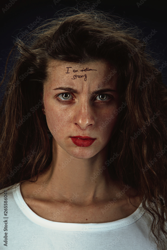 Portrait of young woman overcoming mental health problems. Tattoo on the forehead I am victim-strong. Concept of psycological trouble, treatment, rehabilitation, return to healthy lifestyle. Portrait of young woman overcoming mental health problems. Tattoo on the forehead I am victim-strong. Concept of psycological trouble, treatment, rehabilitation, return to healthy lifestyle.