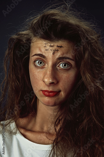 Portrait of young woman with mental health problems. Tattoo on the forehead with the words I feel good-all right. Concept of hidding the true feelings  psycological trouble  treatment.