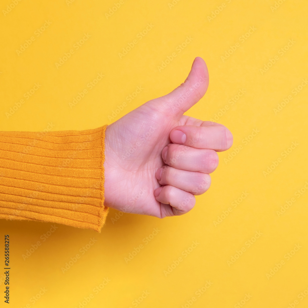 Beautiful woman hand making thumb up gesture on yellow bright background. Like concept