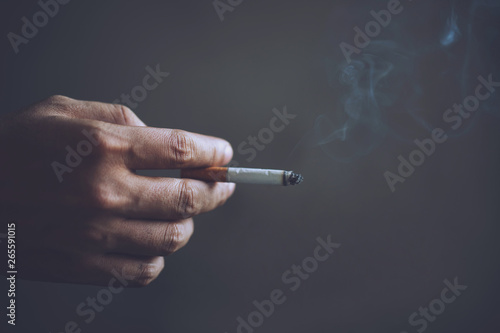 man holding smoking a cigarette in hand. Cigarette smoke spread. dark background