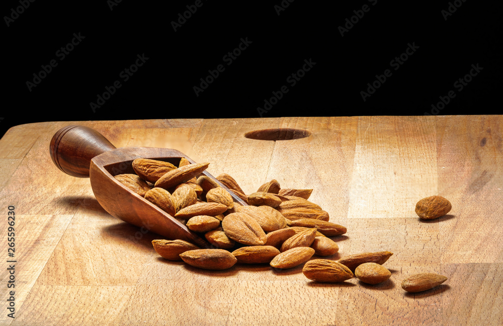 heap of peeled almonds in a wooden spoon on table blurred black background