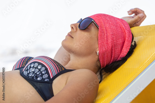 Woman sunbathing and relaxing on yellow sunbed, tanned female with black sunglasses