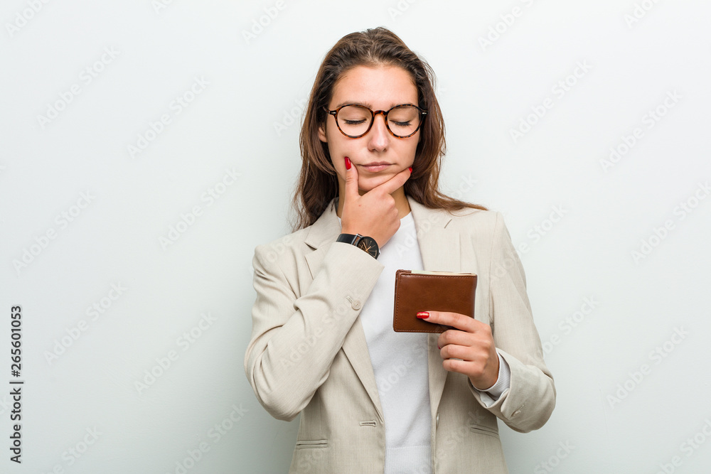 Young european business woman holding a wallet looking sideways with doubtful and skeptical expression. Young european business woman holding a wallet looking sideways with doubtful and skeptical expression.