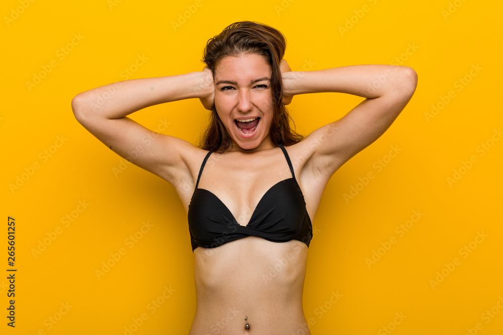 Young european woman wearing bikini covering her ears with hands trying not to hear too loud sound. Young european woman wearing bikini covering her ears with hands trying not to hear too loud sound.