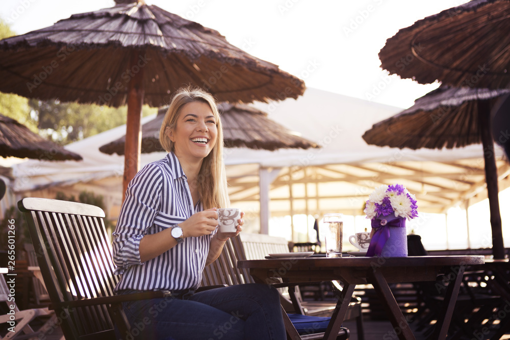 A beautiful young blonde drinks coffee and laughs at the restaurant by the sea, she gets flowers for a present and is very happy.