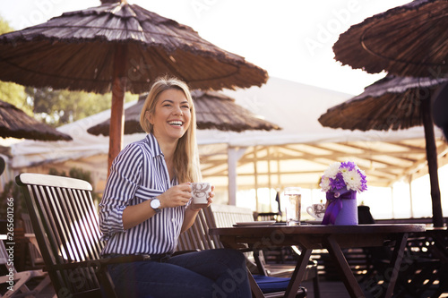 A beautiful young blonde drinks coffee and laughs at the restaurant by the sea, she gets flowers for a present and is very happy. © borevina