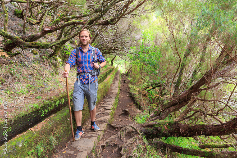 Beautiful landscape view of a young handsome tourist on the hiking path in nature on the green island Madeira, during a hike on a trail along a famous levada