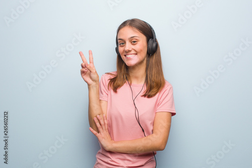 Young pretty caucasian woman showing number two. She is listening to music with headphones.