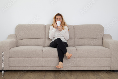 Caucasian blonde woman sitting on a sofa drinking her morning coffee, casual and relaxed
