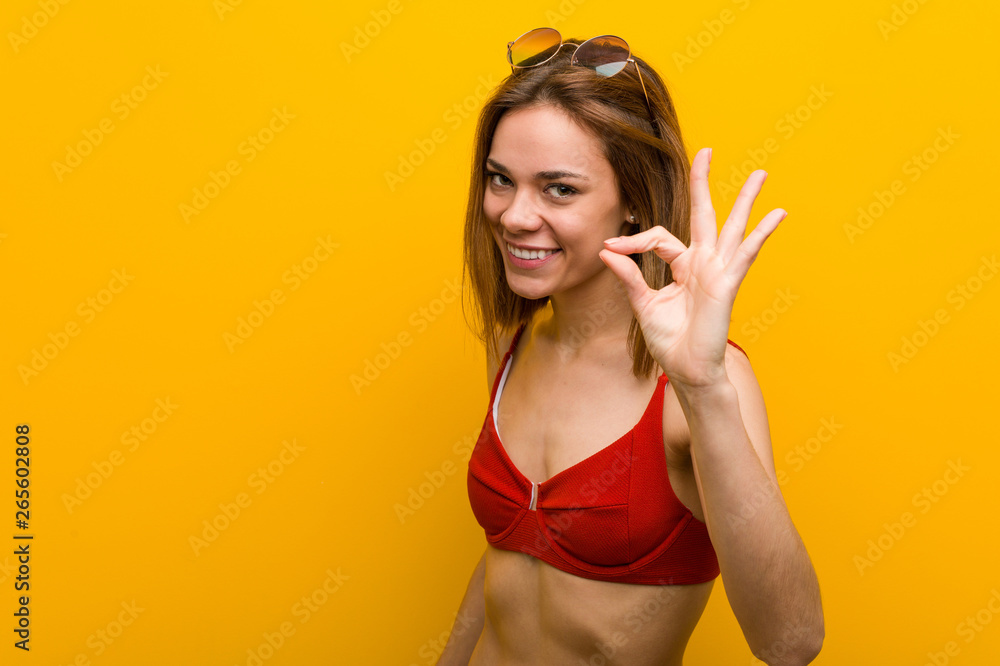 Young caucasian woman wearing bikini and sunglasses cheerful and confident showing ok gesture. Young caucasian woman wearing bikini and sunglasses cheerful and confident showing ok gesture.