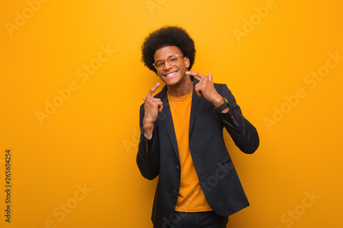 Young business african american man over an orange wall smiles, pointing mouth