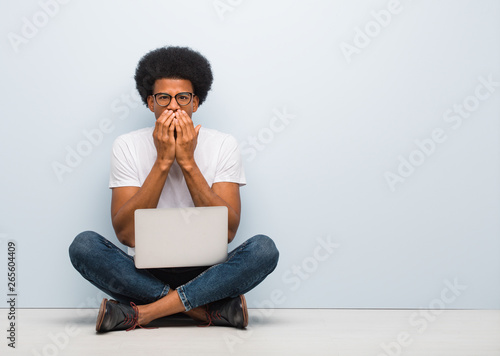 Young black man sitting on the floor with a laptop very scared and afraid hidden