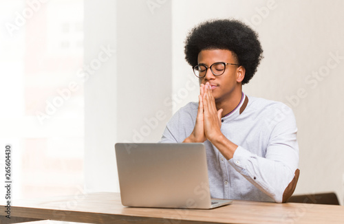 Young black man using his laptop praying very happy and confident