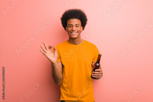 Young african american man holding a beer cheerful and confident doing ok gesture