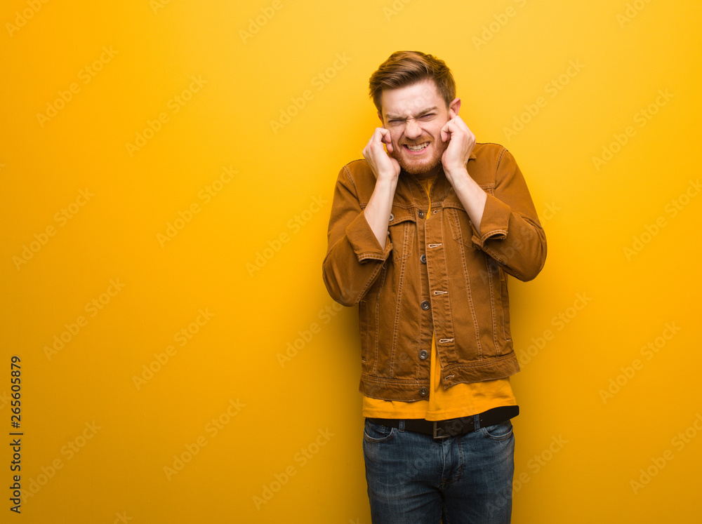 Young redhead man covering ears with hands