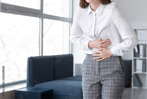 Young woman suffering from abdominal pain in office © Pixel-Shot