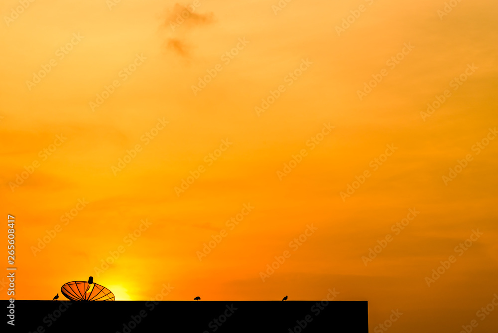 Silhouette of old satellite dish on building with a yellow sky background