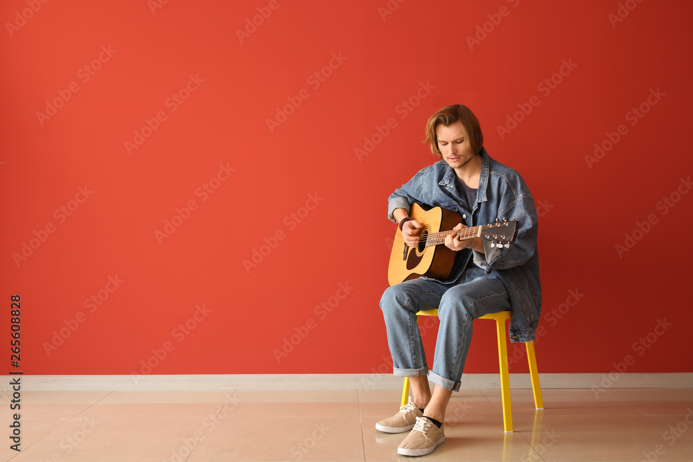 Handsome young man playing guitar near color wall Handsome young man playing guitar near color wall