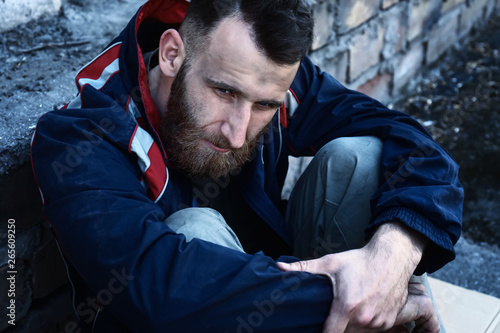 Poor homeless man sitting near wall outdoors photo