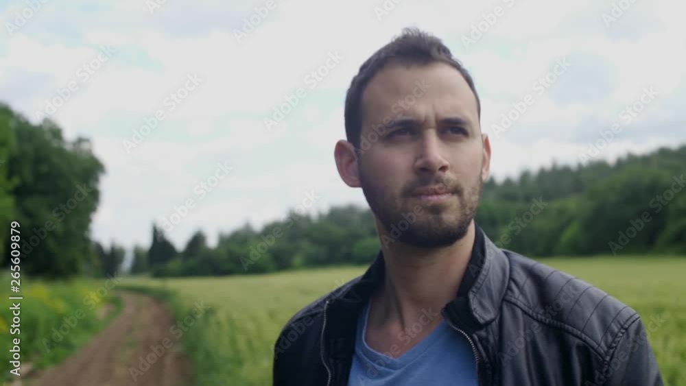 Man with a jacket looking serious in an empty country road with fields in background Man with a jacket looking serious in an empty country road with fields in background