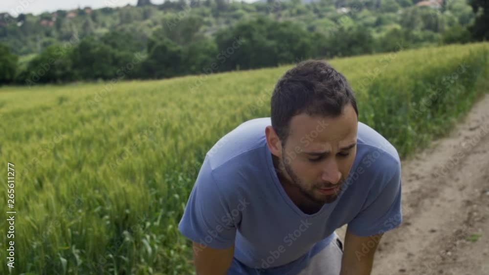 Man in jogging clothes is tired after a run taking deep breaths while standing in countryside Man in jogging clothes is tired after a run taking deep breaths while standing in countryside