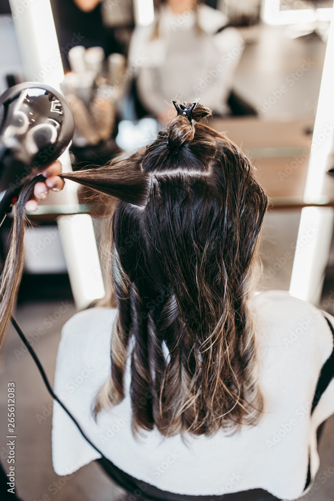 Naklejka premium Beautiful brunette woman with long hair at the beauty salon getting a hair blowing. Hair salon styling concept.