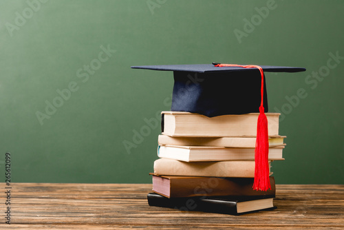 books and academic cap on wooden surface isolated on green