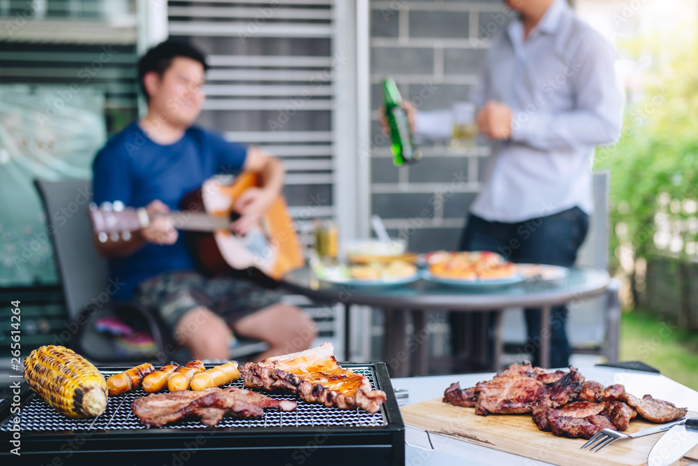 Group of friends Two young man enjoying grilled meat and play guitar with raise a glass of beer to celebrate the holiday festival happy drinking beer outdoors and enjoyment at home