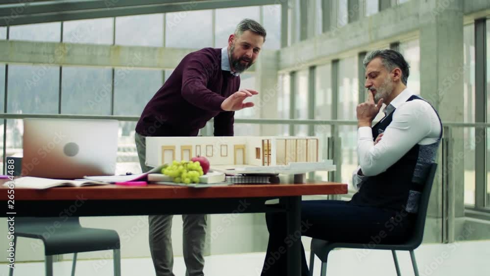 Two architects with model of a house standing in office, talking. Two architects with model of a house standing in office, talking.