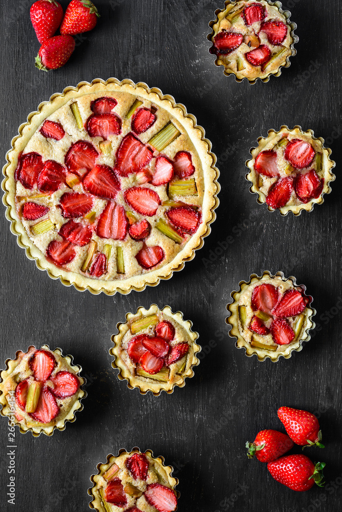 Homemade tarts with strawberry and rhubarb on black wooden background. Top view. Rustic style Homemade tarts with strawberry and rhubarb on black wooden background. Top view. Rustic style